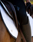 A close up of a rider on a chestnut horse with a white saddle pad and Jackie&Co Lucky Numbers pin.