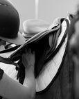 A rider adjusting the saddle with a white Jackie&Co saddle pad under it.