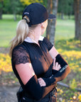 Woman in a sunny forested area wearing a black outfit styled with black UV protecting arm sleeves and cap.