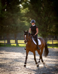 A rider in a paddock on a sunny day with a white saddle pad.