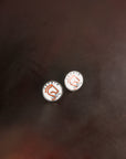 Two white Jackie&Co lucky number pins resting on a dark brown saddle.