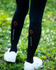 Black Jackie&Co riding socks with and orange line art horse logo on the top of the calf. Worn over black leggings with white sneakers.