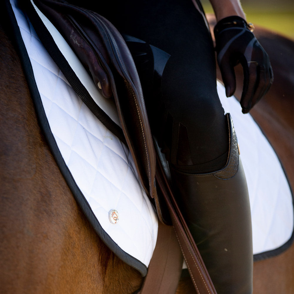 A close up of a rider on a chestnut horse with a white saddle pad and Jackie&Co Lucky Numbers pin. 
