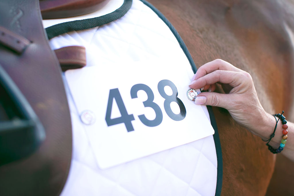 Jackie&Co lucky number pins being used to pin a competition number to a saddle pad on a chestnut horse. 